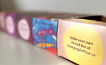 Load image into Gallery viewer, A row of period boxes the front on is in focus and says Order your own period box at changingtheflow.ca. The rest of the row is progressively more blurry. 

