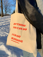 Load image into Gallery viewer, image of our canvas totes that says Anything You Can Do I Can Do Bleeding shown hanging on someone&#39;s shoulder, with snow on the ground in the background
