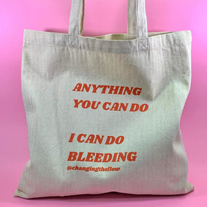 Image of a canvas tote with red writing that says Anything You Can Do, I Can Do Bleeding @changingtheflow