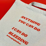 Load image into Gallery viewer, an image of our canvas tote, flatttened on a red background. The writing on the tote is in red and says Anything You Can Do I Can Do Bleeding @changingtheflow
