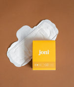 Load image into Gallery viewer, A joni bamboo pad laid out on a light brown background with a yellow box of joni day pads resting on a portion of the pad
