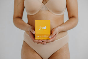 Person wearing beige bra and underwear holding a yellow box of joni bamboo day pads